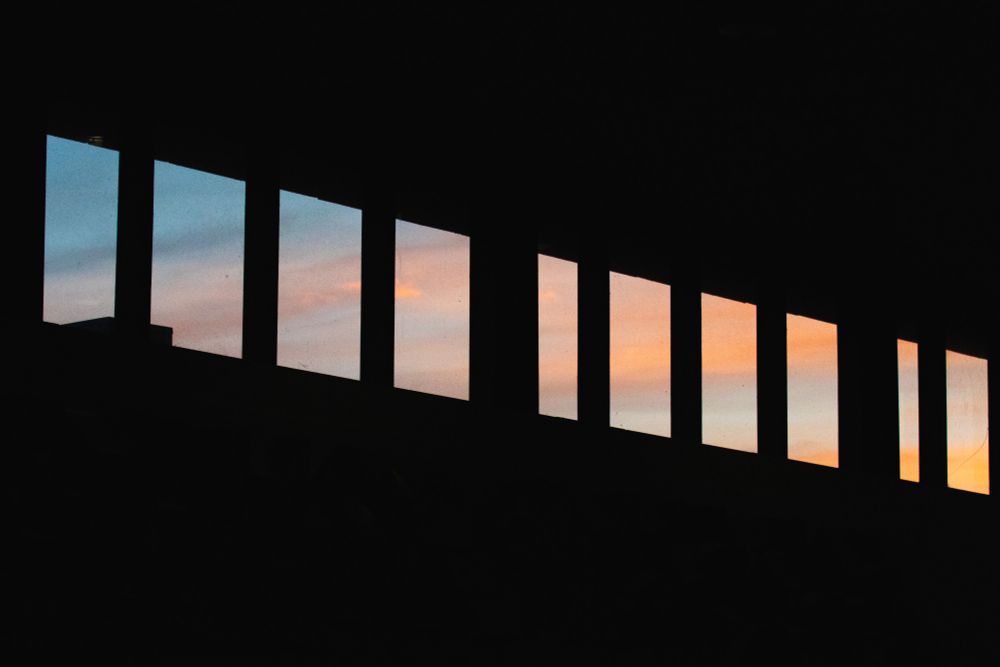 A photograph of a sunset taken from inside a building. The colours of the sunset are the only colours present in the image. The interior of the building is shadowed and black. 