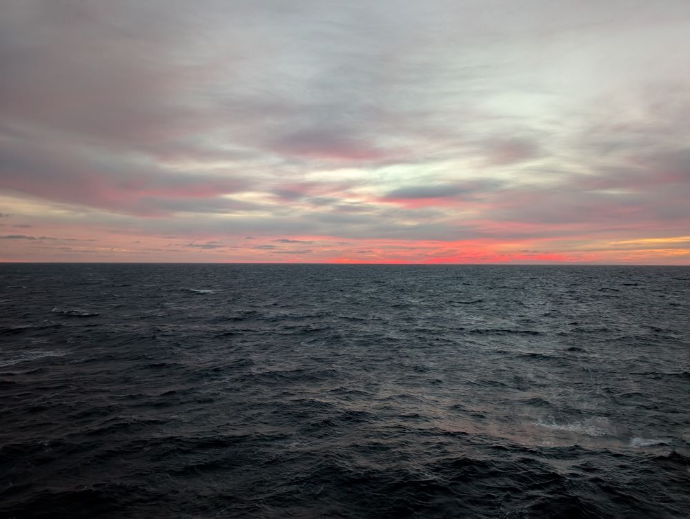 A low layer of clouds reflects a harsh, red sunlight from our star unseen over the horizon