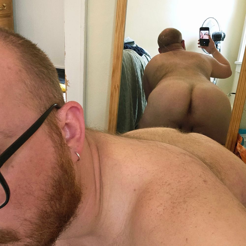 Mirror selfie of hairy ass and back in the background, side of face, ginger beard, and freckled shoulders in the foreground.