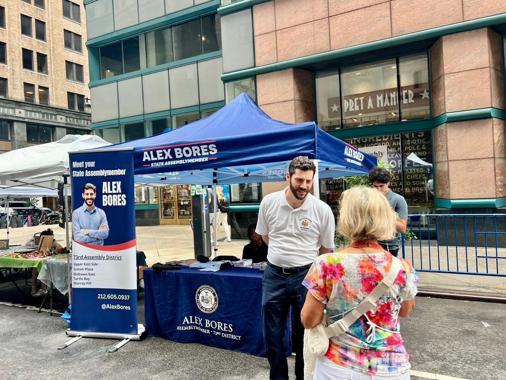 Assemblymember Bores talking with a constituent at a street fair booth.