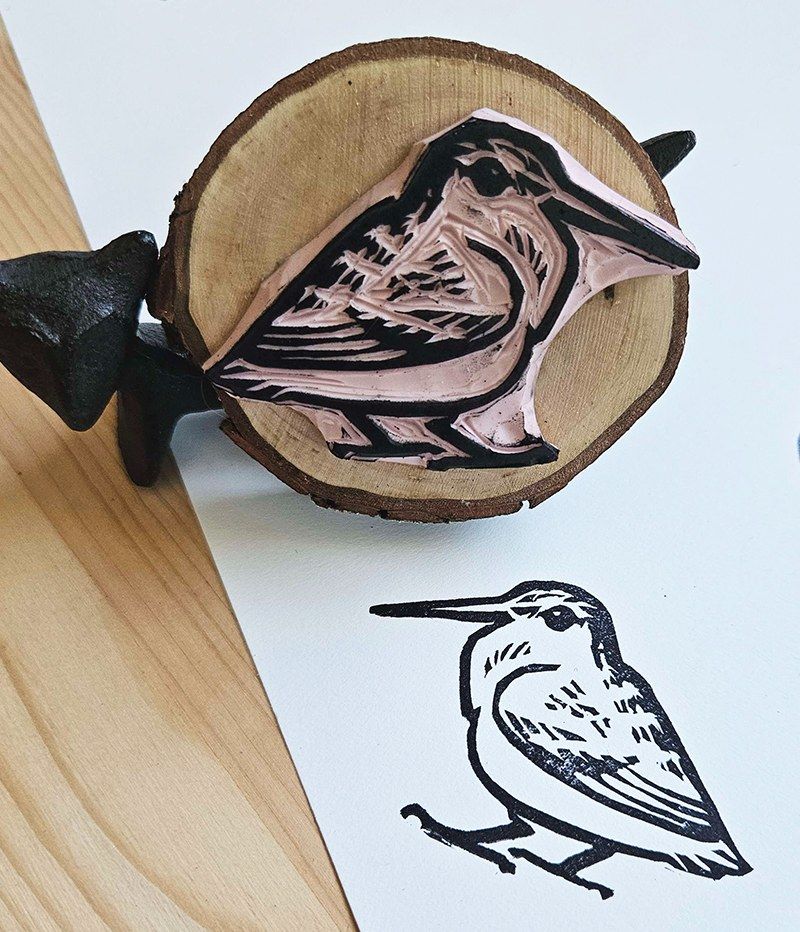 linoleum block stamp of a woodcock mounted to a wooden round, with a print of the stamp in black ink next to it.
