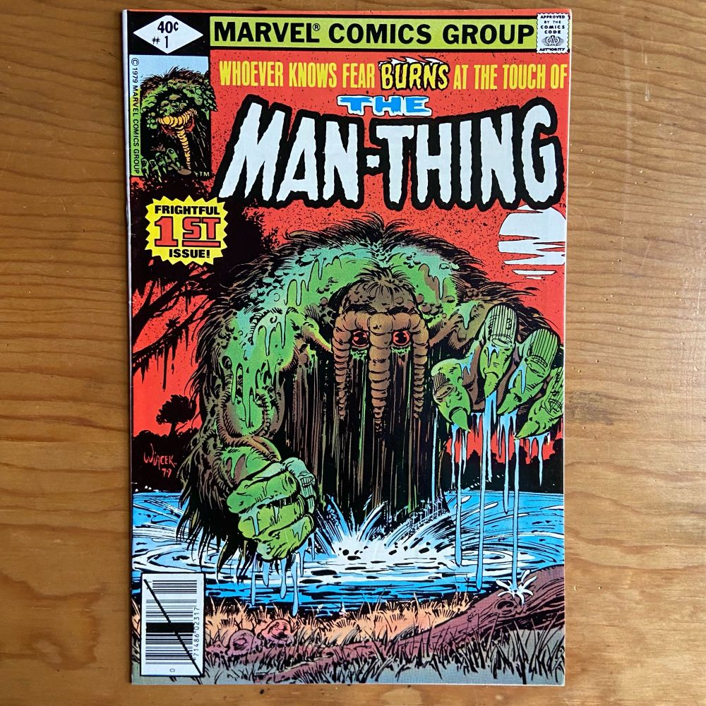 A comic book of The Man-Thing (volume 1, number 1). Cover has an illustration of a swamp like creature emerging from water and reaching out with its large claw hand to grab the reader