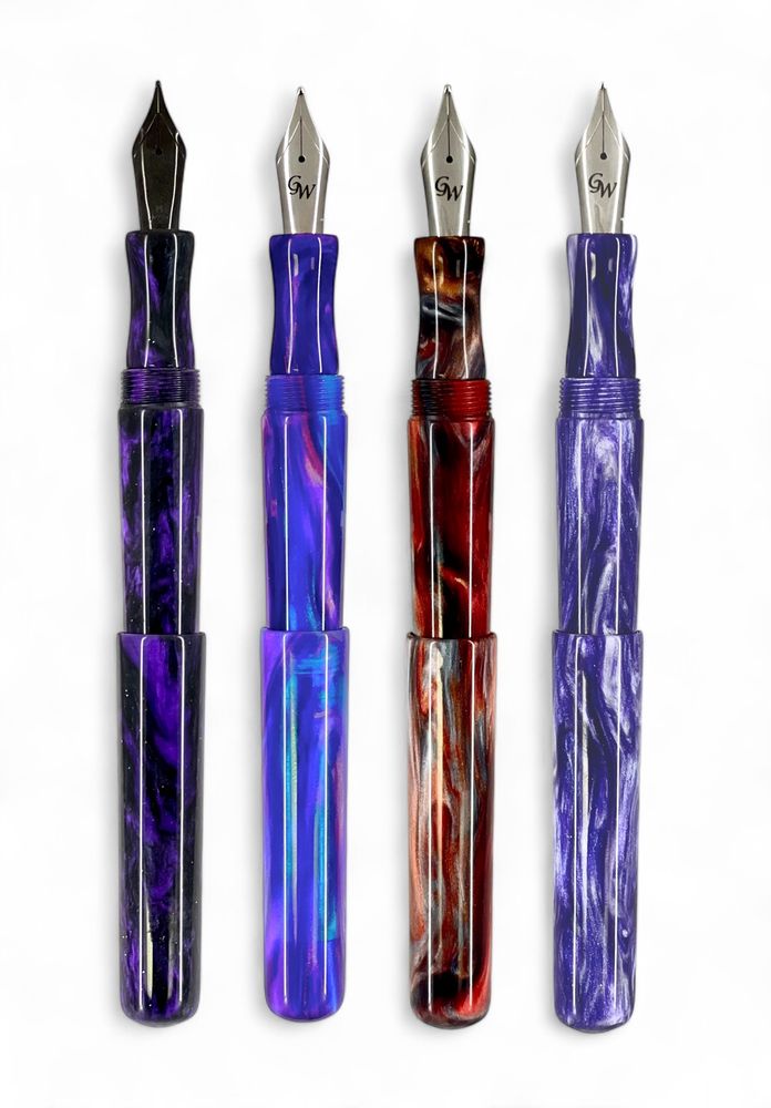 Four GW D2 fountain pens are shown with caps posted against a white background. A black nib in a purple and black resin pen, a steel nib in a purple, pink, and translucent blue pen, a steel nib in a copper-red, silver, and bronze resin pen, and a steel nib in a purple and white resin pen.