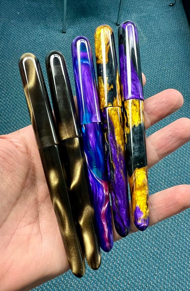 5 resin fountain pens are held in an open hand, capped. 