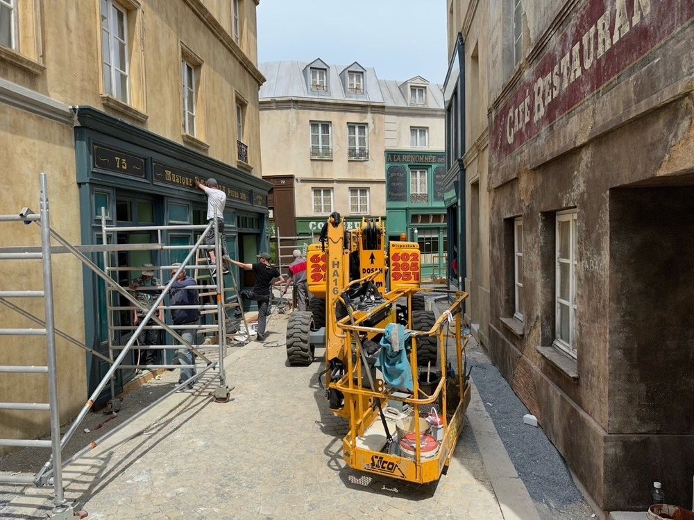Parisian street backlot, filled with scaffolding, construction equipment and crew members hard at work.