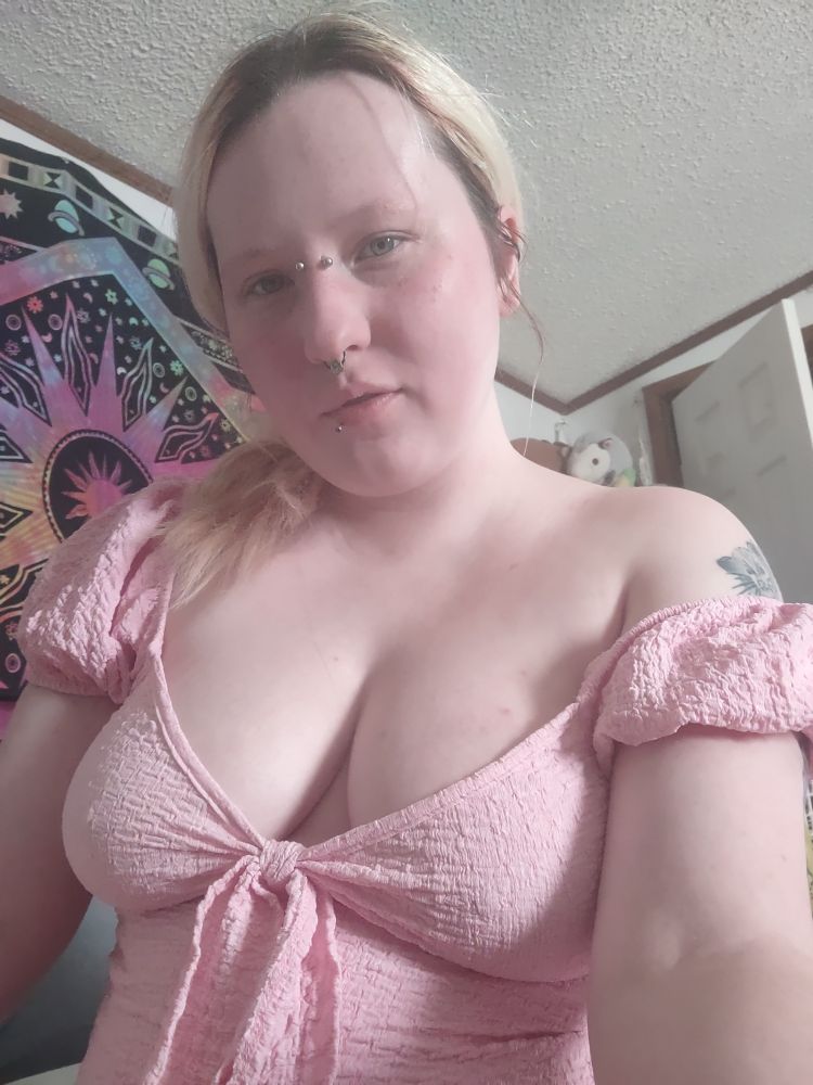 Lori a white nonbinary afab person with bleached hair, blue eyes, and a bridge, septum, and lip piercing is wearing a tight low cute light pink sundress. 