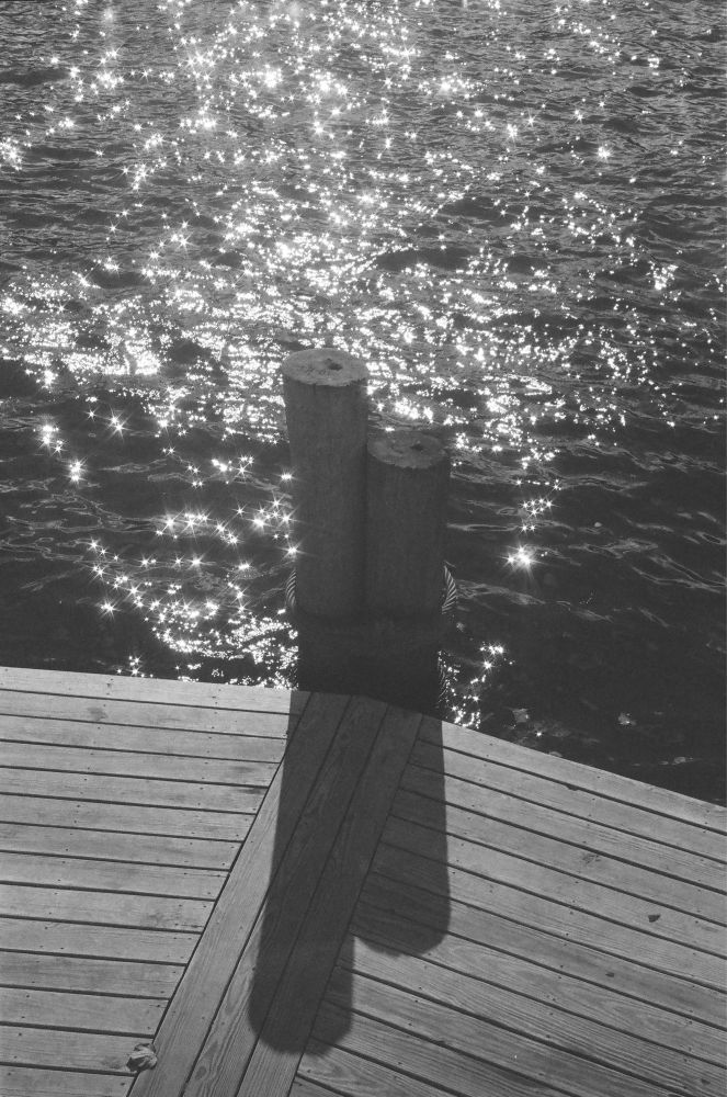 A black and white image of a small dock against a sparkling river.