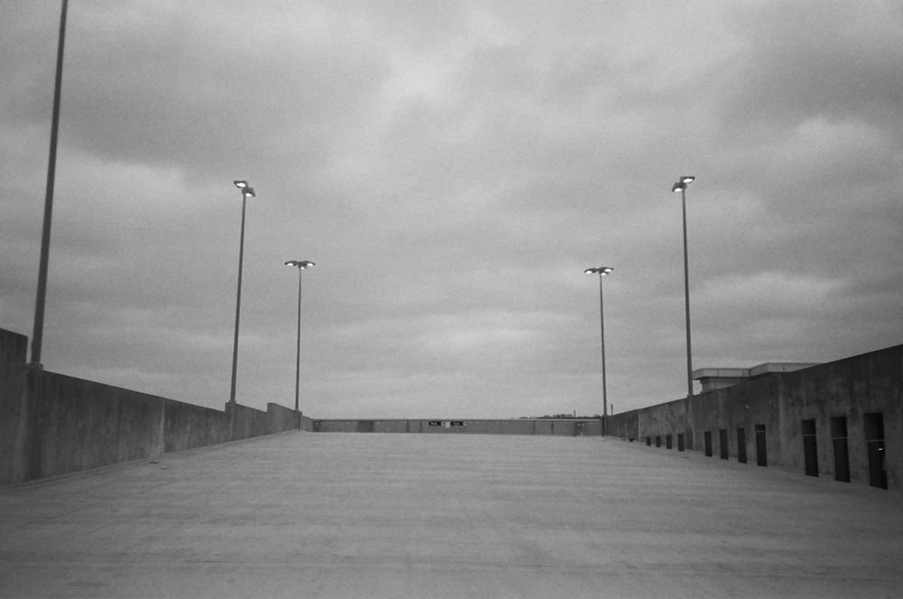A black and white photo of the top of a parking garage ramp and light posts.