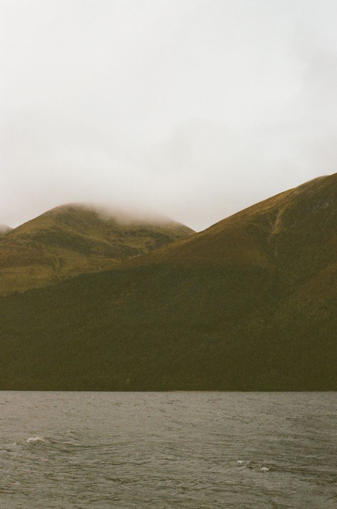 A grainy color photograph of a foggy Scotland landscape with a few small mountains and river.
