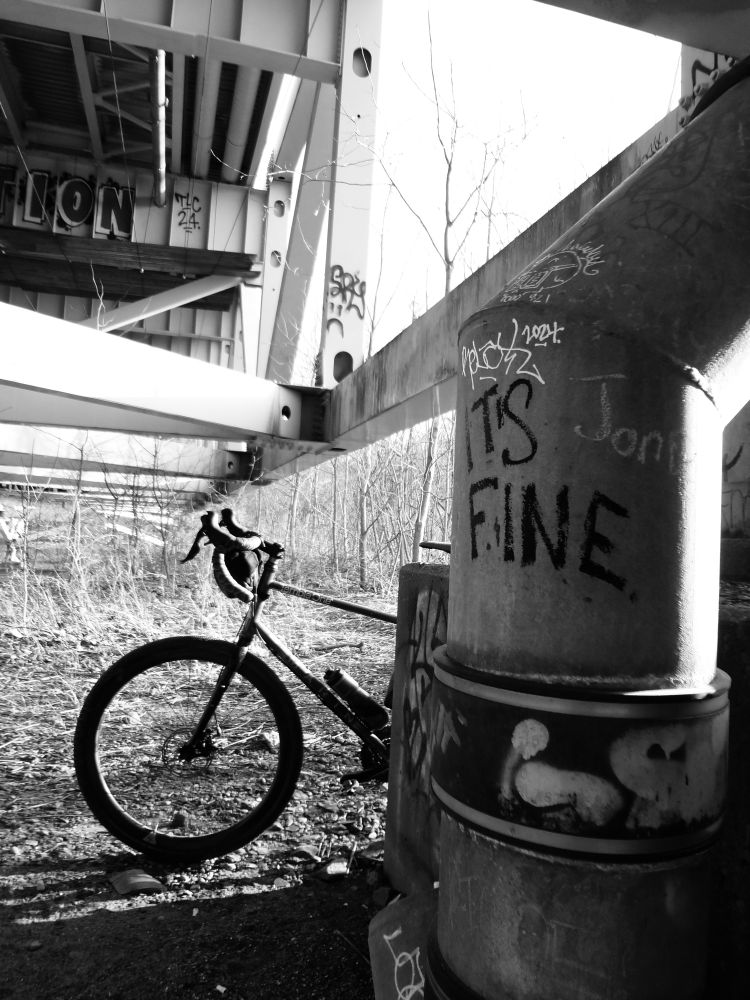 A black and white photo of graffiti saying “It’s Fine” with a bike in the background.