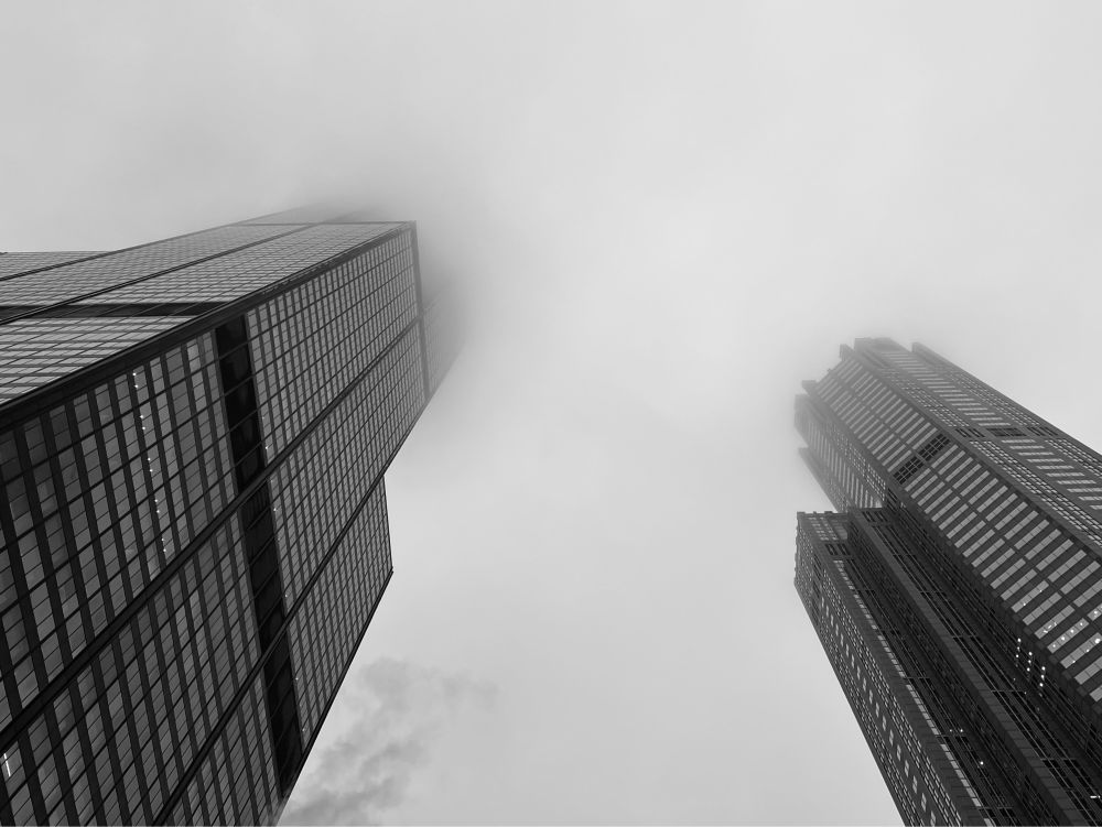 A black and white image of two Chicago buildings in the fog from the sidewalk looking up.