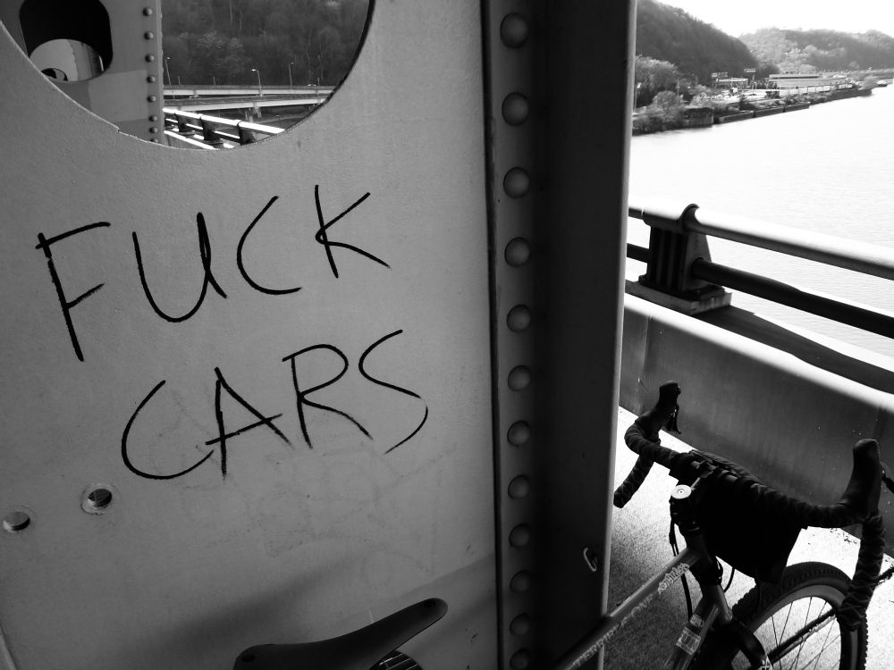 A black and white image of graffiti on a bridge with a bicycle slightly in view.