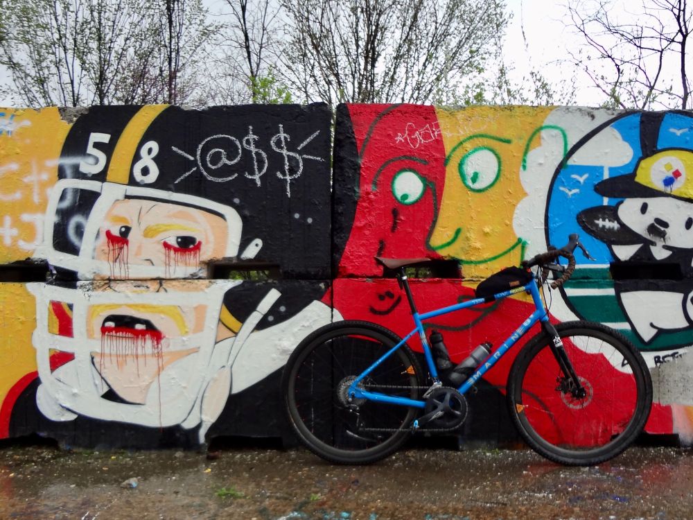 A blue bicycle leaning up again concrete blocks with graffiti of a bloody Pittsburgh Steelers football player on it.