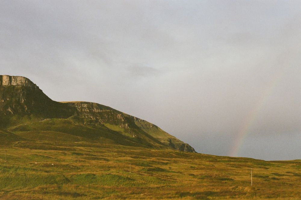 A rainbow meets the landscape over cloudy skies in Scotland.