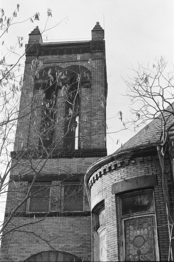 A black and white vertical image of a church tower and dead trees.