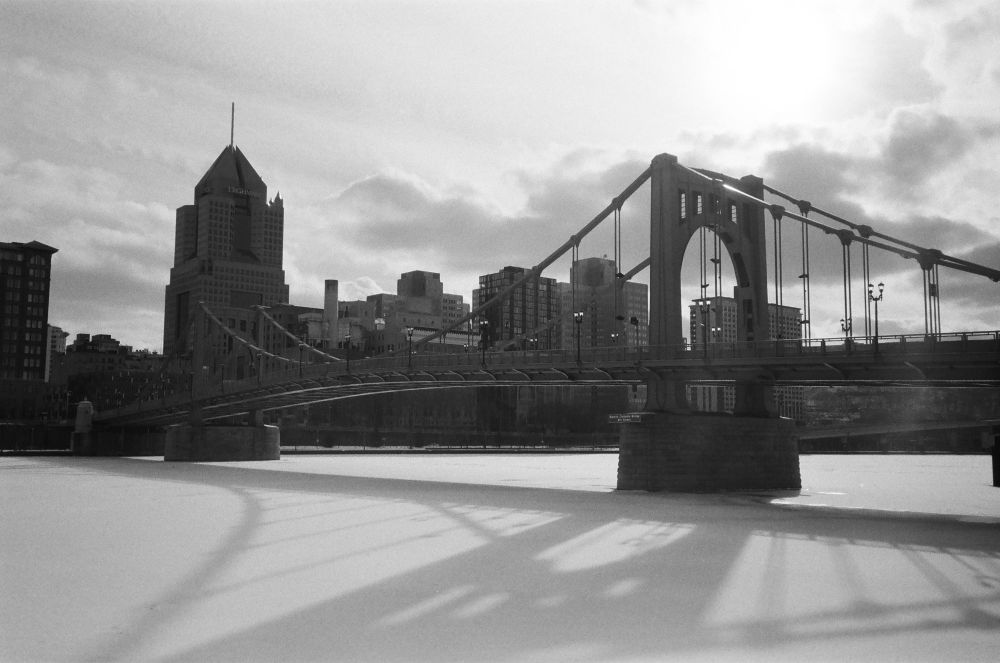 A black and white photo of the Pittsburgh skyline with the frozen, snow-covered river in the foreground.