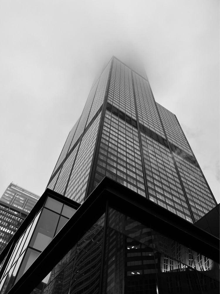 A black and white image of a Chicago building in the fog from the sidewalk looking up.