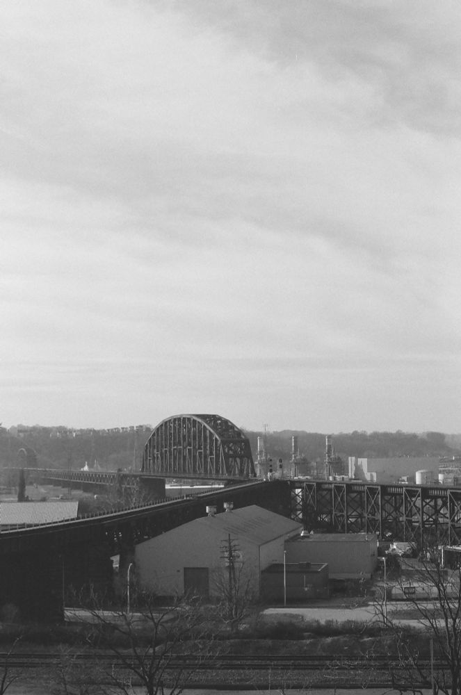 A black and white vertical image of a railroad bridge under a cloudy sky.