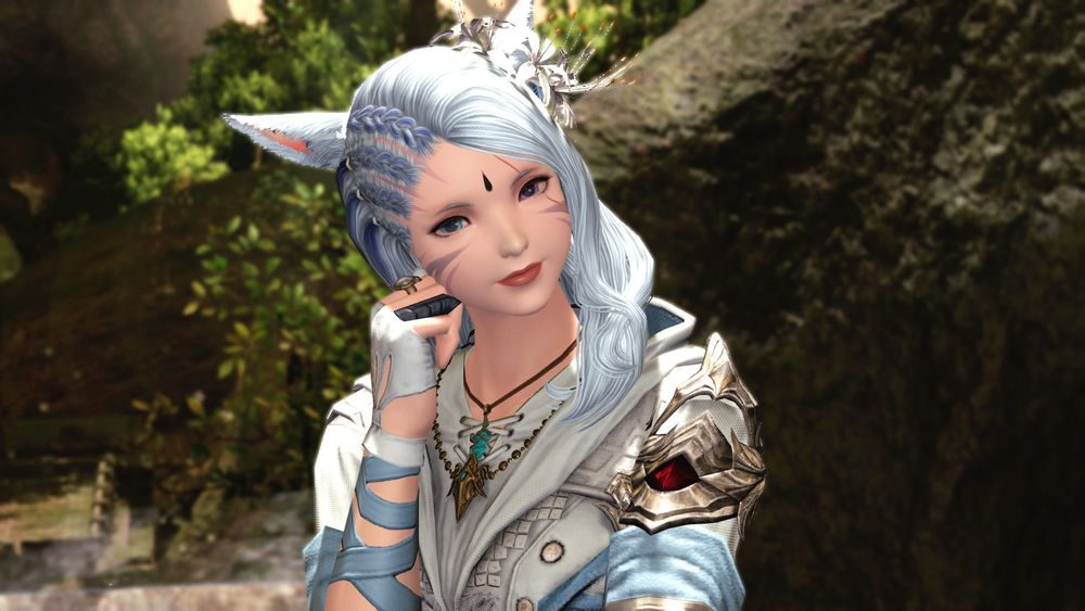A screenshot of a player character from Final Fantasy 14. A Miqo'te woman stands in a forest setting with her hand against her face as she smiles at the camera. 