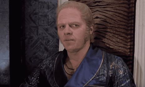 Biff Tannen in Back To the Future 2. He’s wearing a blue silky robe, a five head and weird blonde hair, looking to the right with menace 
