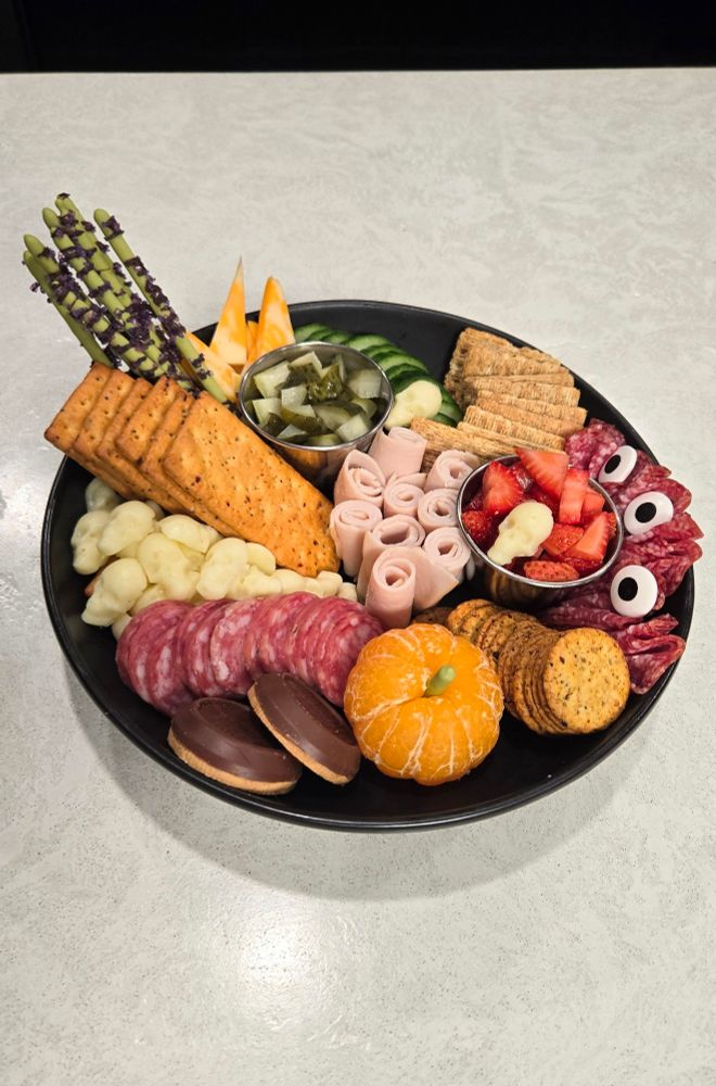 Charcuterie plate, with skull shaped mozzarella, a pumpkin shaped clementine, and candy eyeballs added to the folded salami.