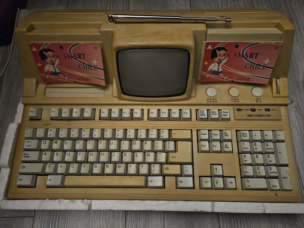 A "Smart Child" video game console, a clone Famicom with a smart built-in CRT screen and a full-sized keyboard. Two cardboard labels on the sides of the screen say "Smart Child 128AE" and show a drawing of a boy who looks like Richie Rich but with black hair.