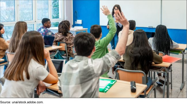 Students sitting at desks raise their hands.