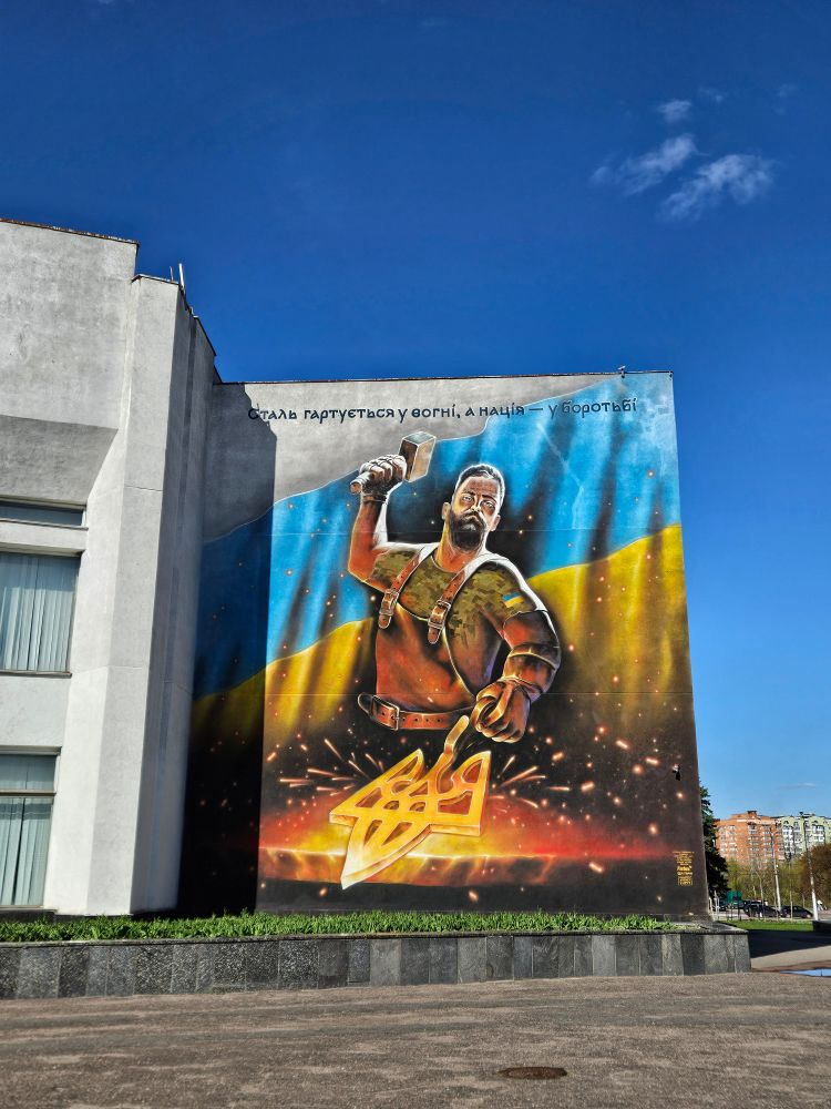 An almost three story high mural of a blacksmith forging the Ukrainian trident over white-hot coals.