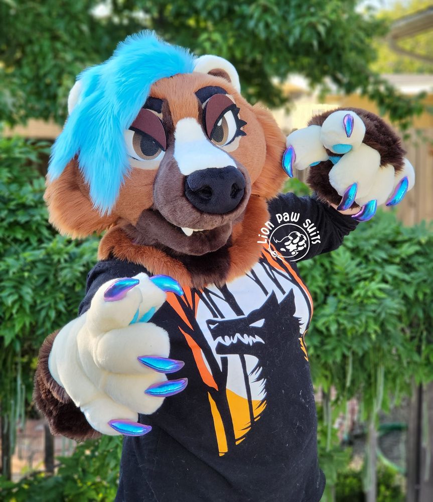 A brown and cream mustelid fursuit with turquoise hair and holographic claws.