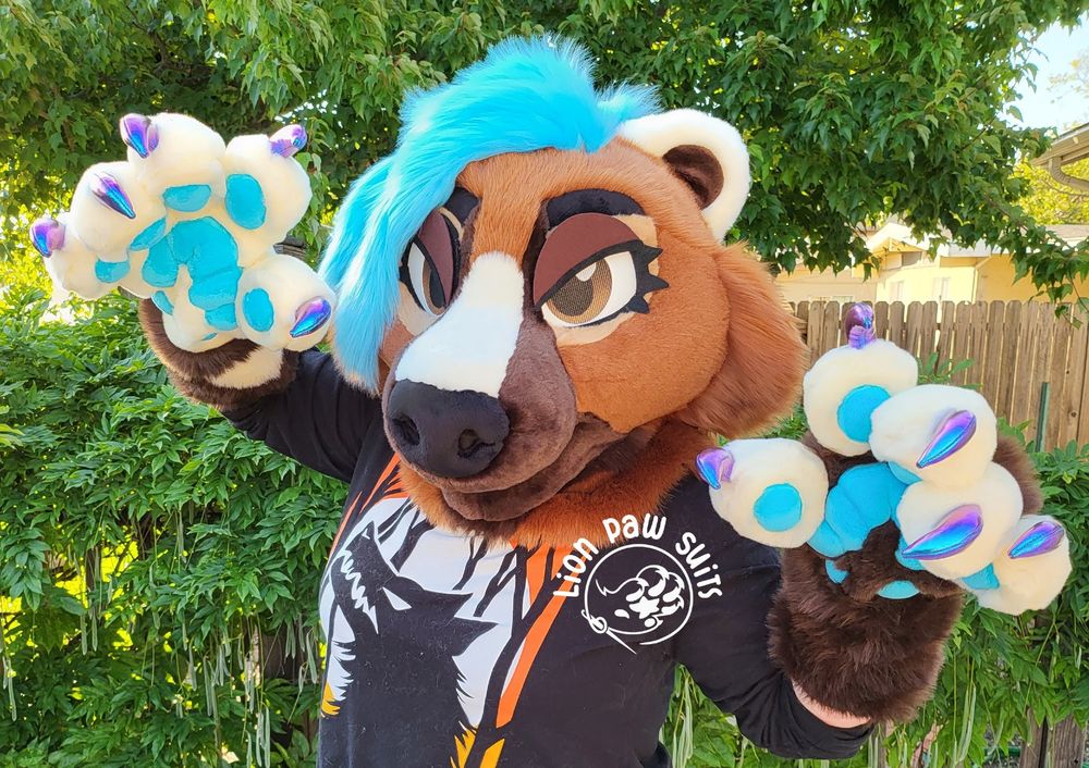 A brown and cream mustelid fursuit with turquoise hair and holographic claws.