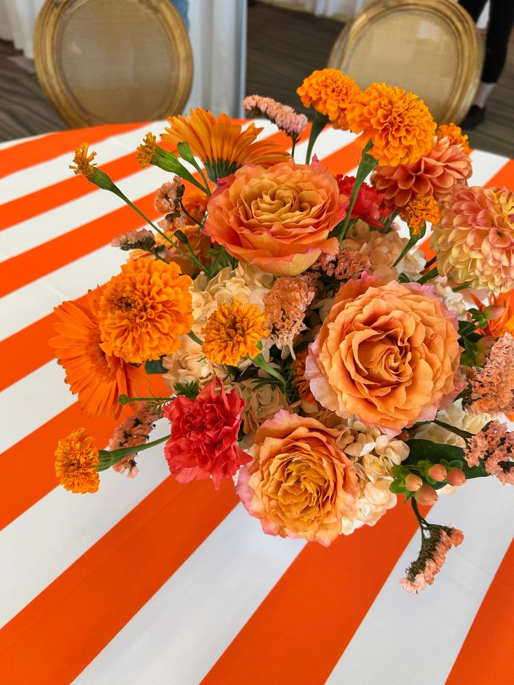 A closeup of a floral arrangement with a variety of orange flowers sitting on an orange and white striped tablecloth