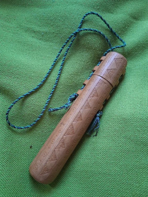 A cylindrical case with a geometric carved design, on a bright green woven cloth background.