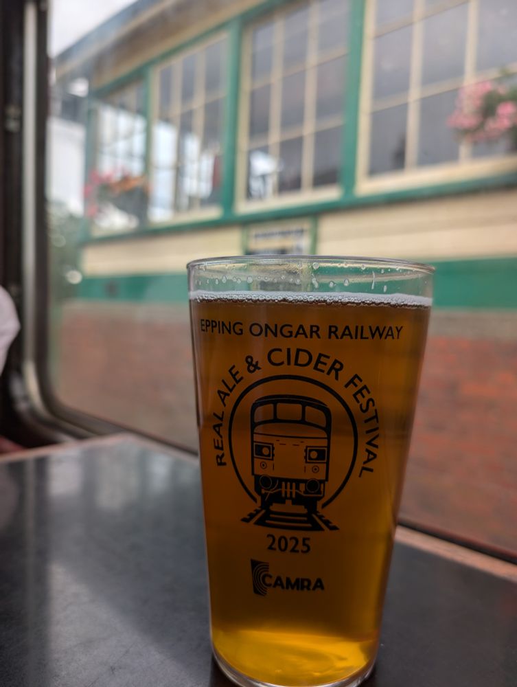 A pint of cask ale in a pint glass that has Real ale & cider festival 2025 printed around a pictogram of an old diesel engine. At the top Epping Ongar Railway is printed.