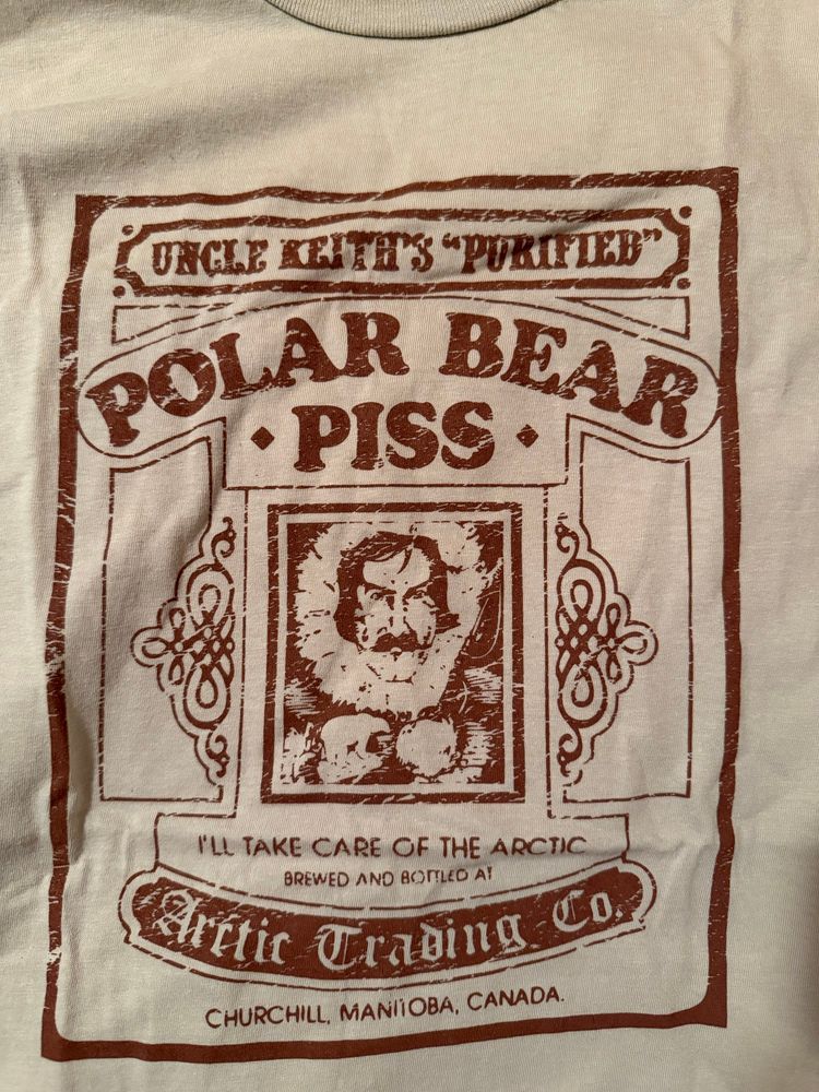 A photo of a graphic T-shirt of an old advertisement for ‘Uncle Keith’s “Purified” Polar Bear Piss”

It’s the name of an alcoholic drink served at the bar next to the Arctic Trading Company (which still currently exists as a gift shop). It’s a sweet, cider-like drink.