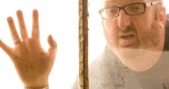 man with his hand splayed on glass and looking through it with an yearning glance 