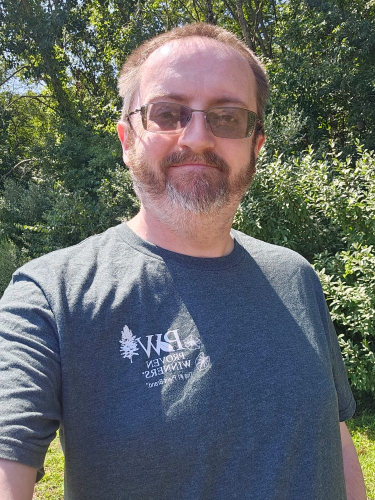 It is me with my usual smirk.  I've got on a grey tshirt and there's trees behind me.