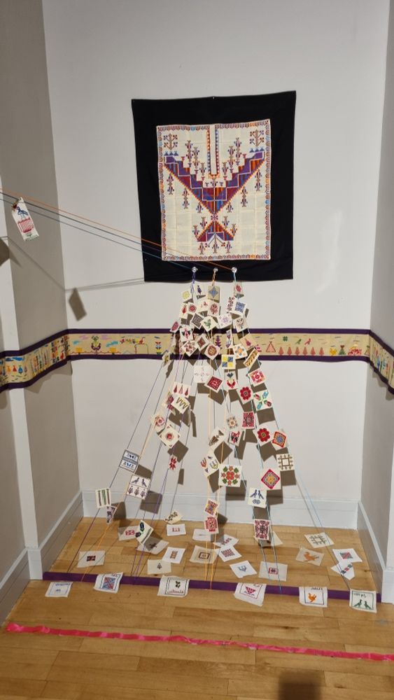 Instalación que simula un thobe, pecho con bordado en forma de collar y falda con piezas de bordado unidas por hilos. 