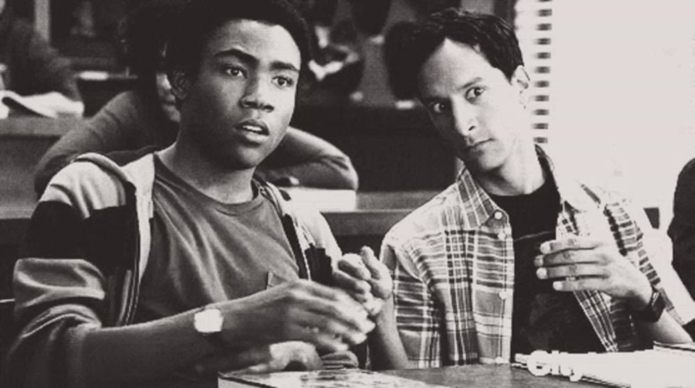 a black and white photo of two young men sitting at a table talking