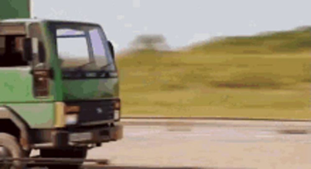 a green truck is driving down a dirt road in a field .