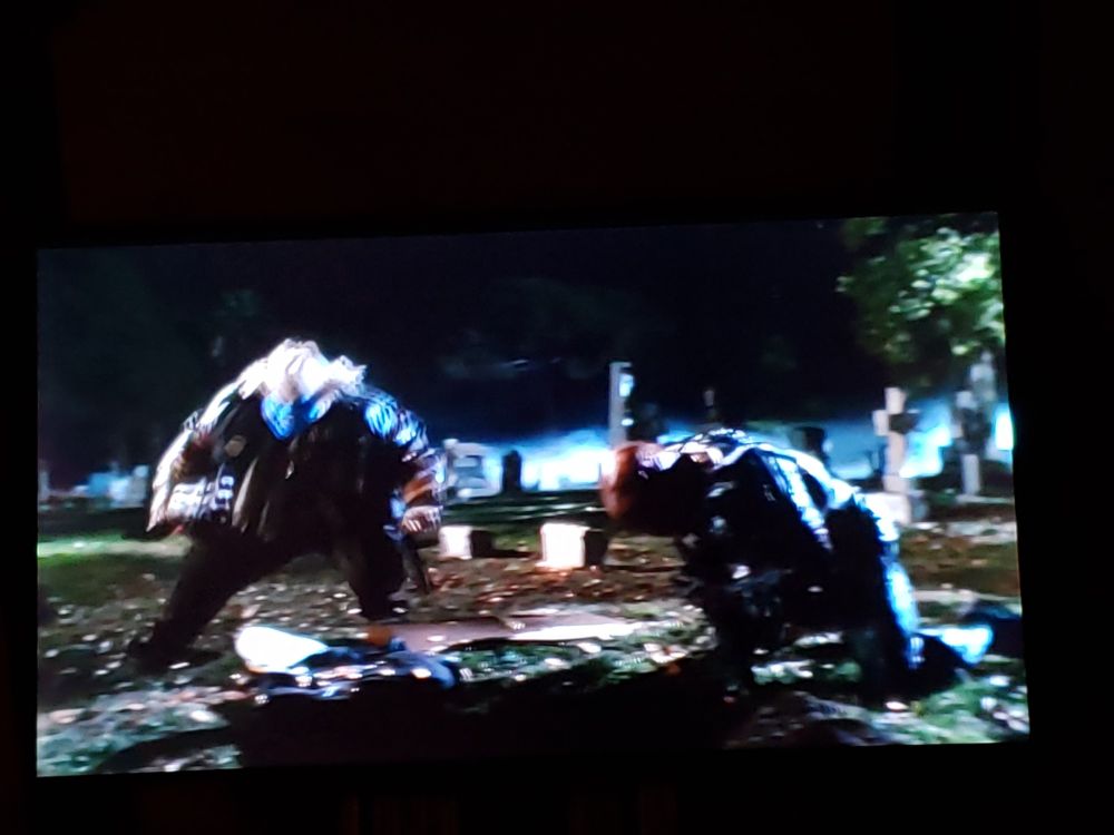 A portly clown man in motion taking big step while flayed man kneels over own grave.

Still from Spawn (1997)