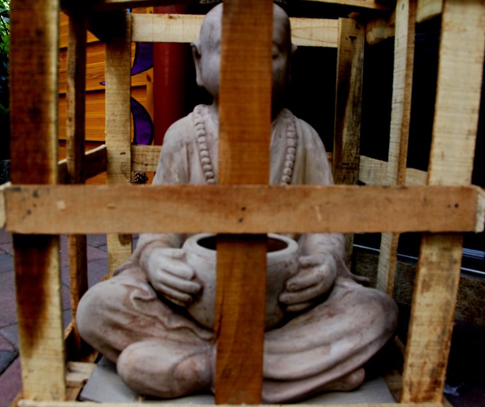 Buddha sitzt in der Kiste & Gefangenschaft. Er hält ein Gefäß zwischen den Beinen fest. Bald wird er albern im Gartenrestaurant herum stehen und die verehrten Gäste werden die Asche ihrer Zigaretten in das Gefäß schnippen. Wir haben den zweiten Advent!