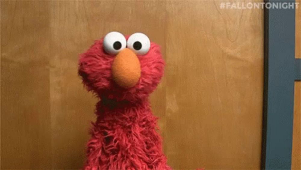 elmo from sesame street is sitting in front of a wooden door .