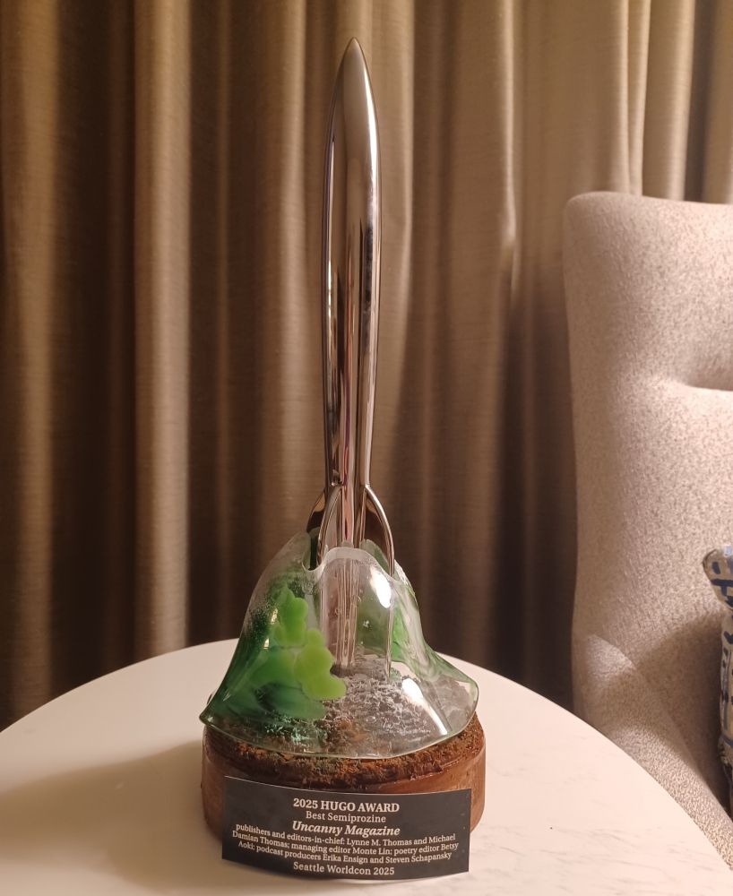 The Hugo Award for Best Semiprozine. Chrome rocket on a wooden base with a fragile glass topper swirled with green and snow. 
