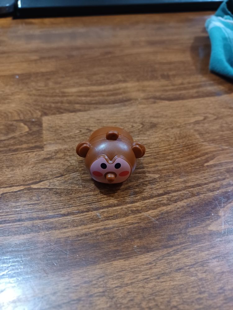 A small, brown, plastic toy on wheels. It has a pink face.
