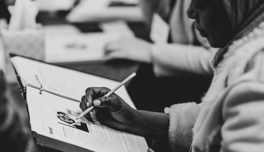 A black and white photo of a woman using a pencil to write on a piece of paper in a binder