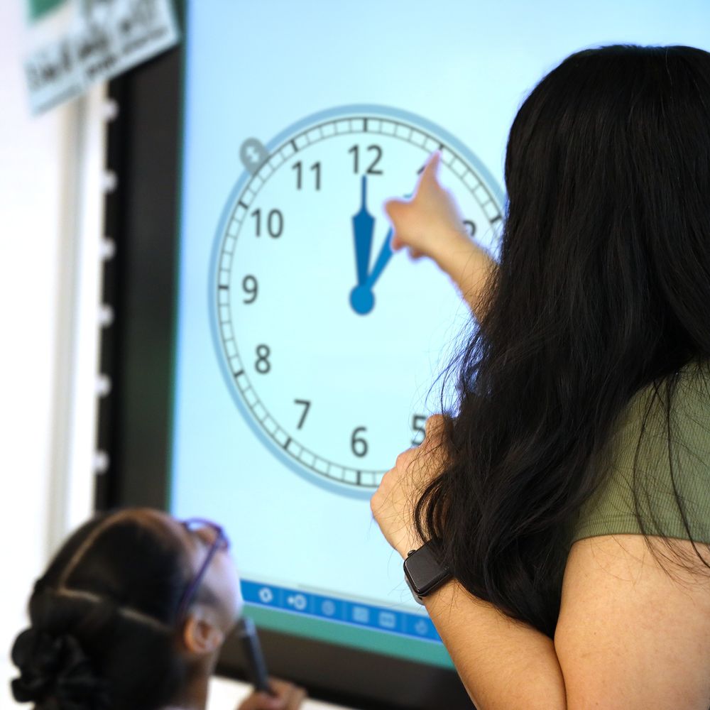 A teacher showing a student a large projected image of the math clock app.