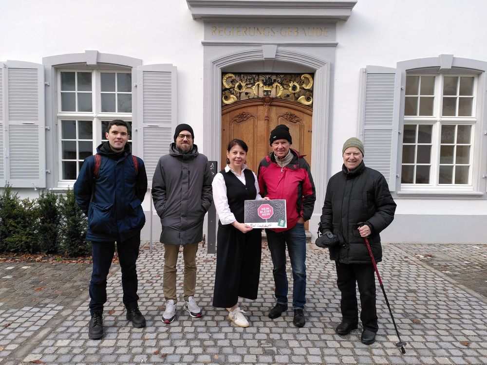 Vier Männer und eine Frau stehen in einer Reihe. Einer der Männer übergibt der Landschreiberin einen Umschlag mit den Petitionsunterschriften. Im Hintergrund ist das Regierungsgebäude in Liestal zu sehen.