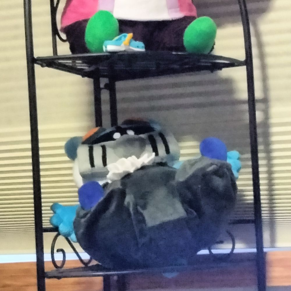 A plush toy sitting up on the shelf of the original posters furry character, Butch, a cyan hamster with a squarish gas mask and dark gray overalls