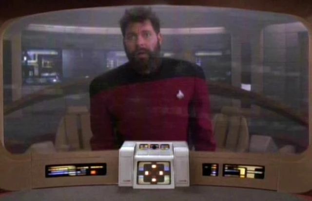 Riker with a scruffy beard looking terrified on the communicator