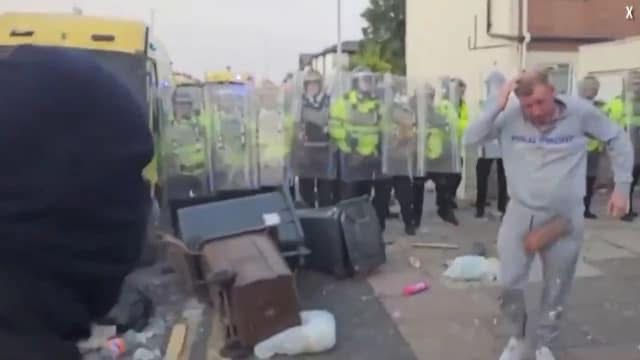 Silly racist rioter dancing in front of a bunch of cops with riot shields 1/25th of a second before the brick hits him. The brick is clearly in frame and cock height